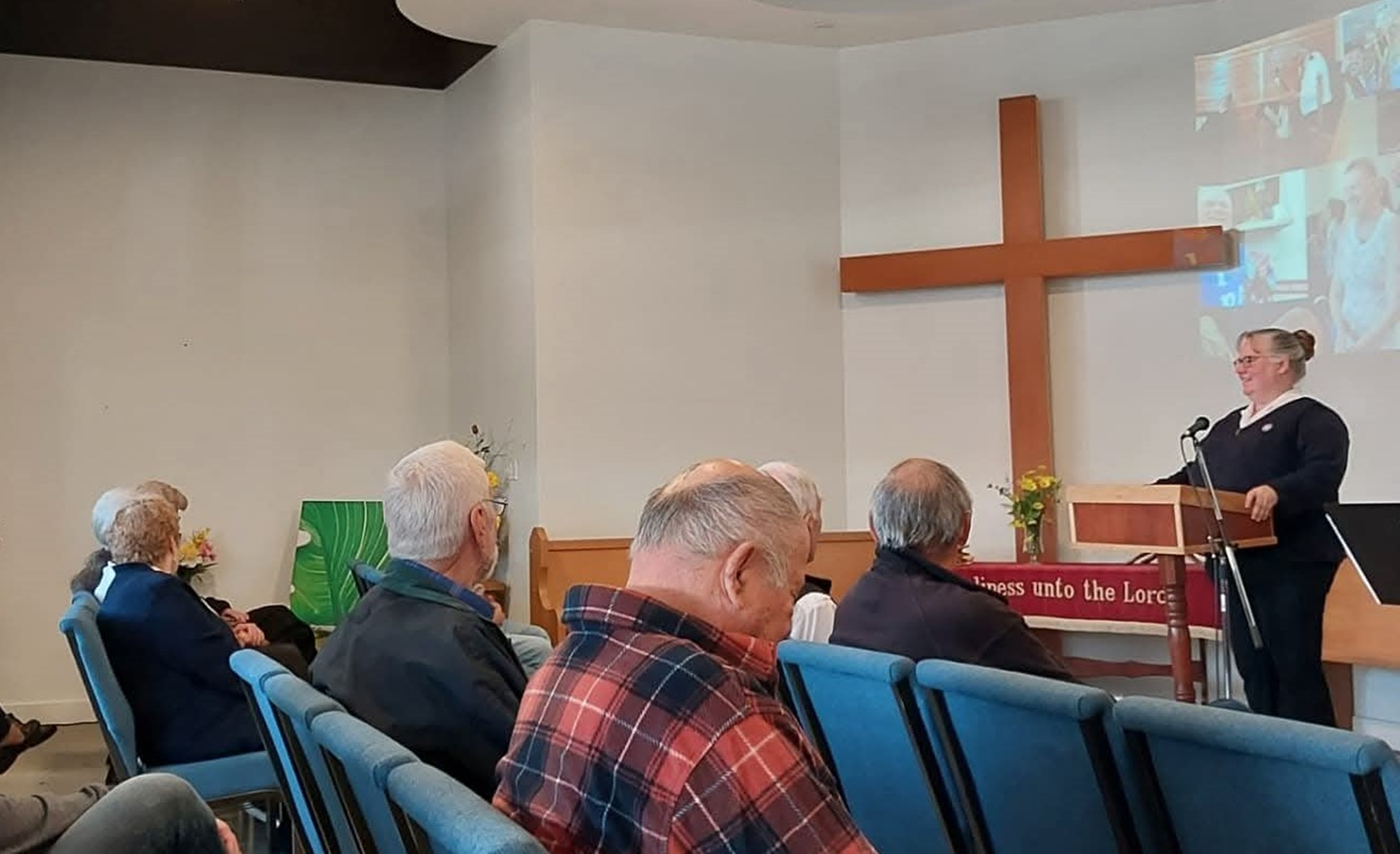 Congregants gathered for the Salvation Army worship service at Alberni Valley Ministries, seated in the sanctuary while a speaker addresses the congregation beneath a cross.