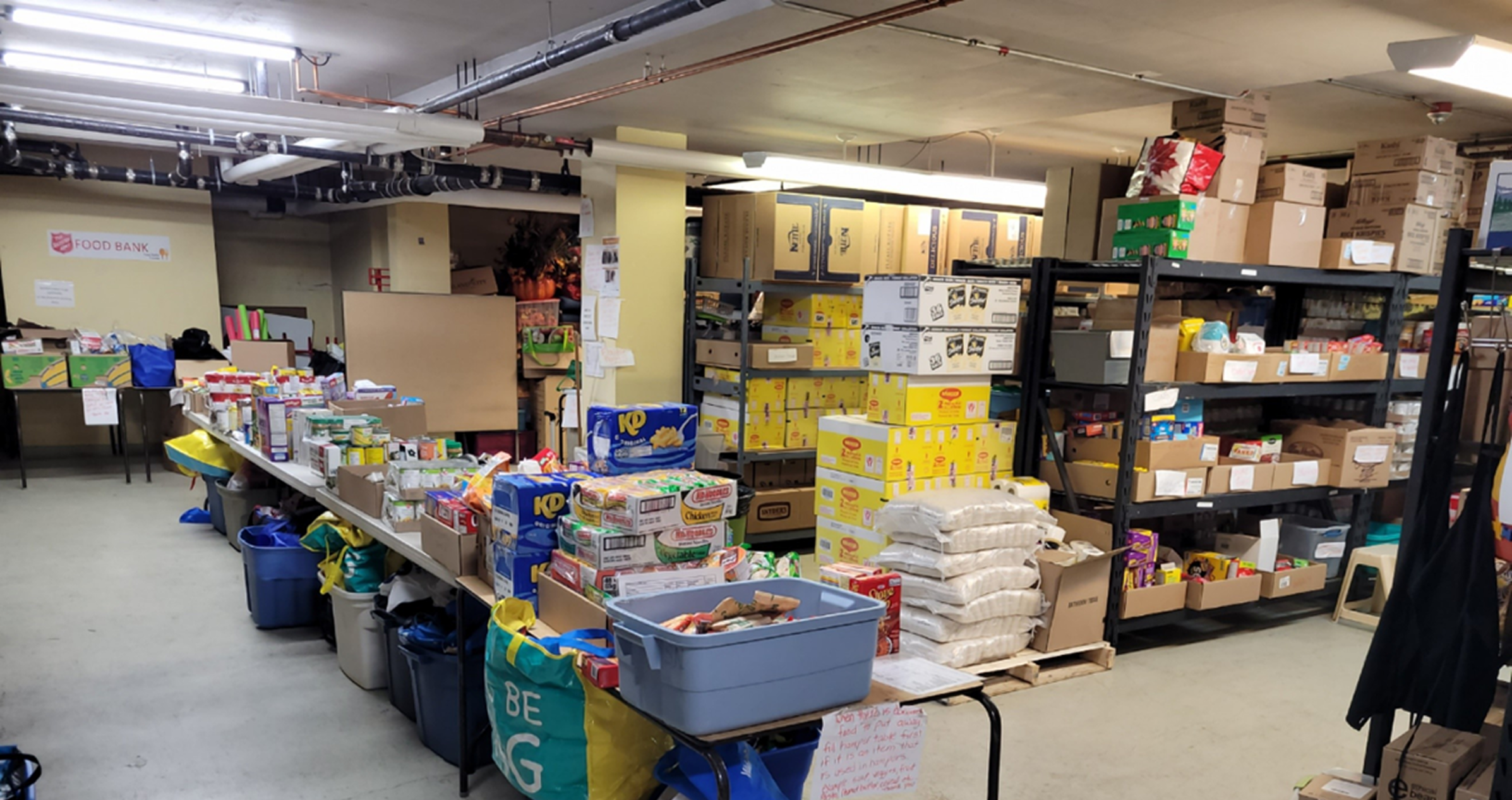 Shelves and tables stocked with packaged food and supplies inside the Alberni Valley Ministries community food bank, prepared for distribution to individuals and families.