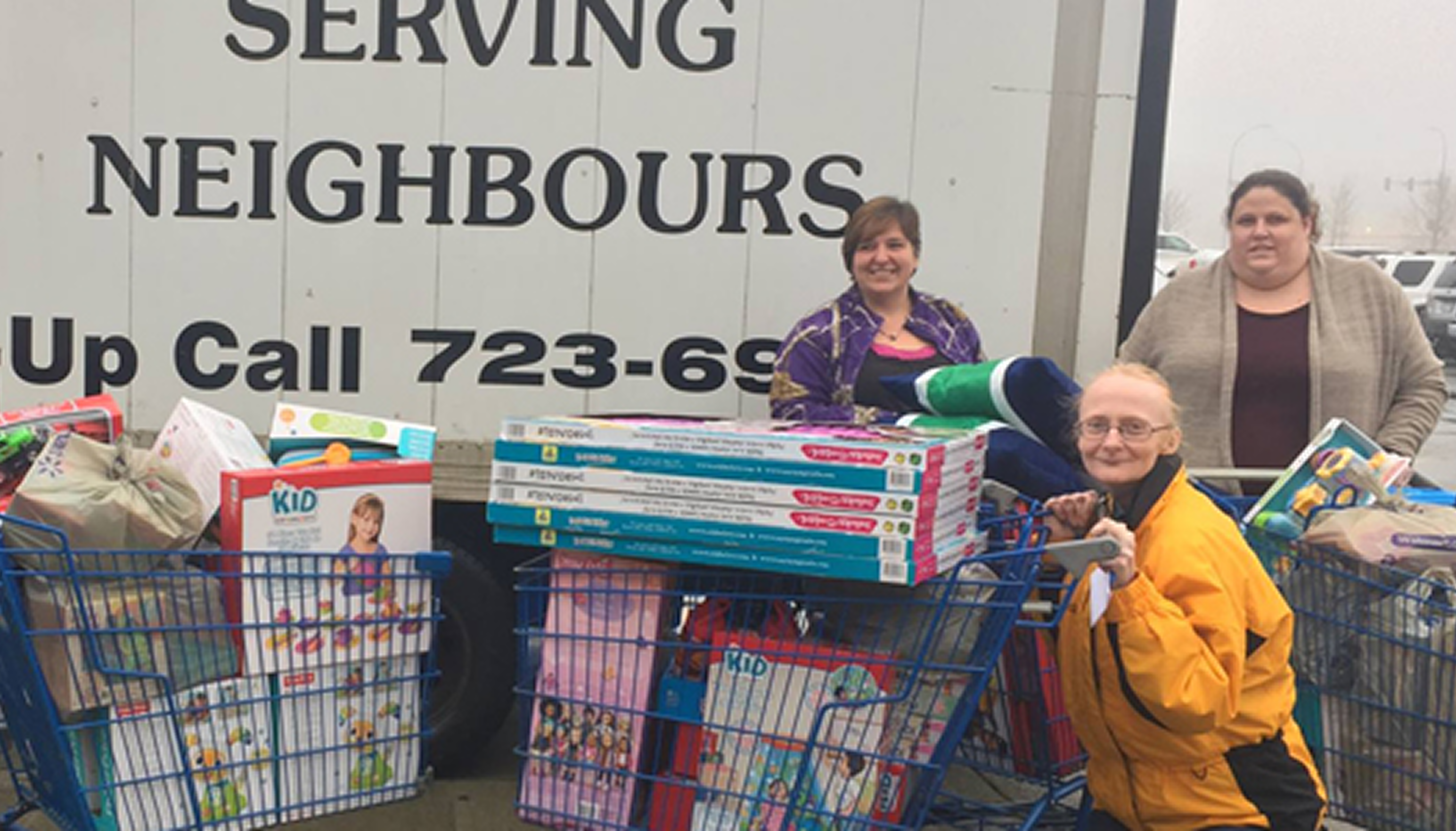 Community members and the Salvation Army volunteers stand outside a building with shopping carts filled with food, diapers, and household supplies.